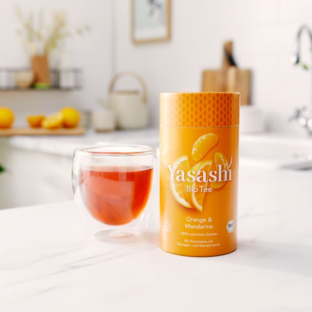 Yasashí Teedose in orange mit Bio Früchtetee mit Orangen und Mandarinenöl. Daneben Tee eingefüllt in einem Thermo Glas